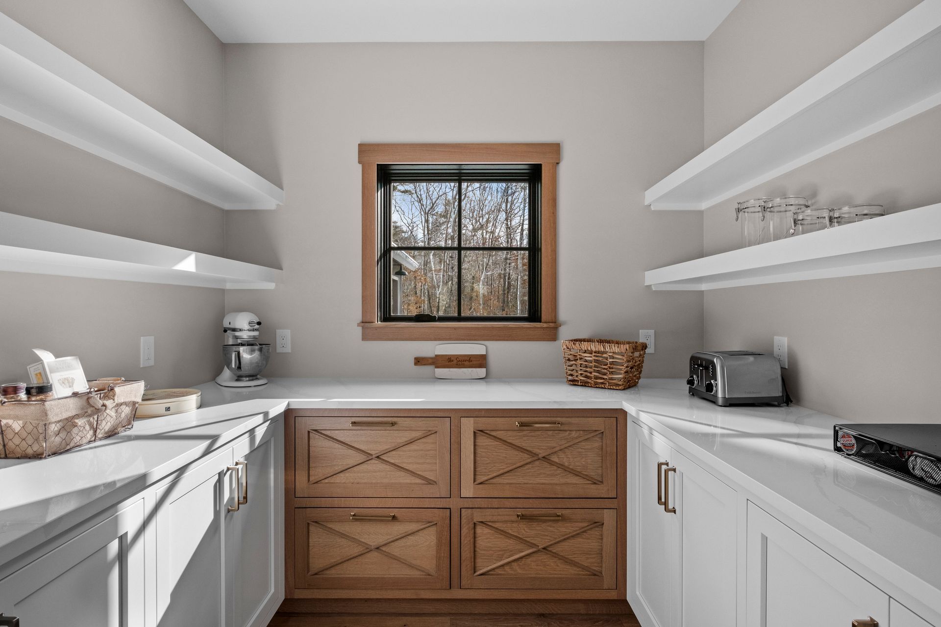 Pantry with light wood cabinets, white countertops, and open shelving. A small window looks outside.