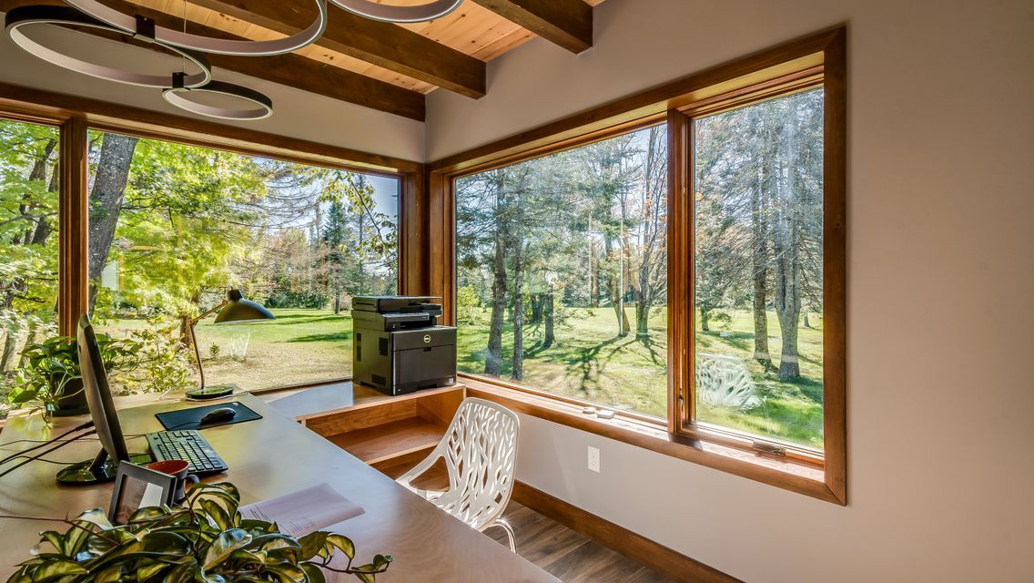 A home office with a desk , chair , computer , printer and large windows.