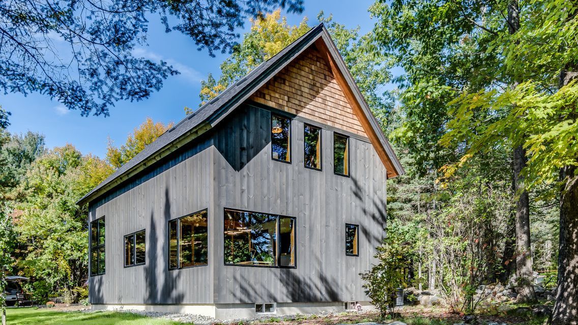 A black house with a wooden roof is surrounded by trees.