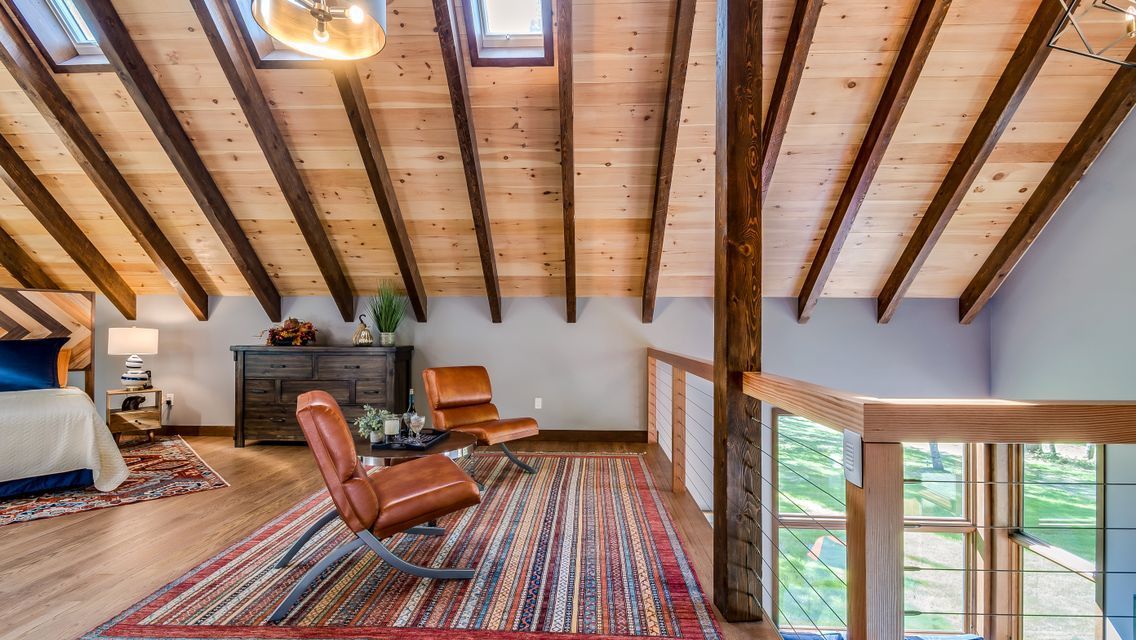 A living room with a wooden ceiling , chairs , a rug and a bed.