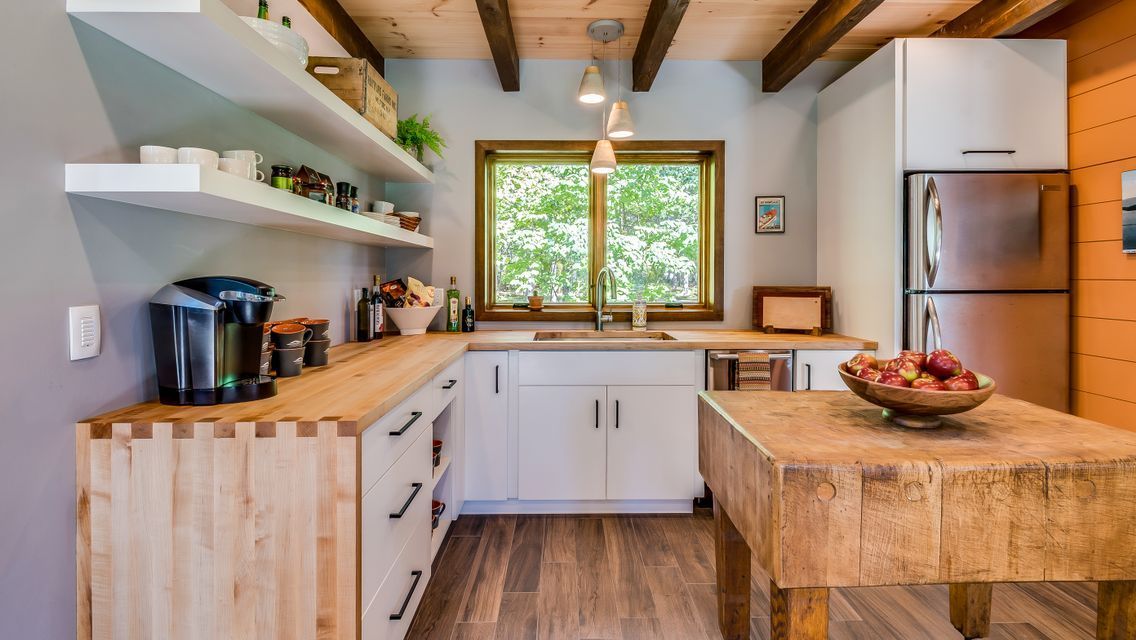 A kitchen with wooden cabinets , a wooden table , a refrigerator , and a window.