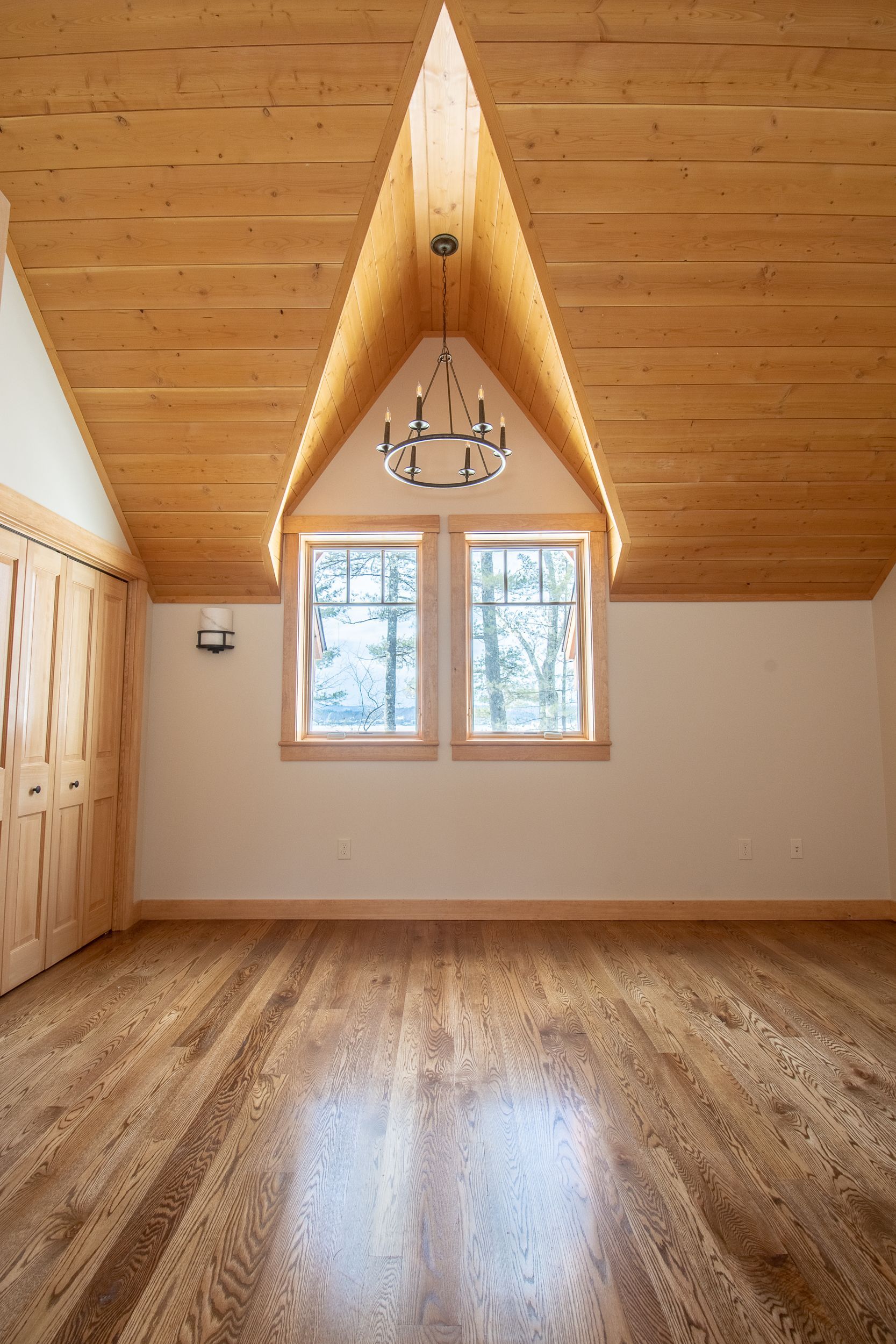 An empty room with a wooden floor and a chandelier hanging from the ceiling.