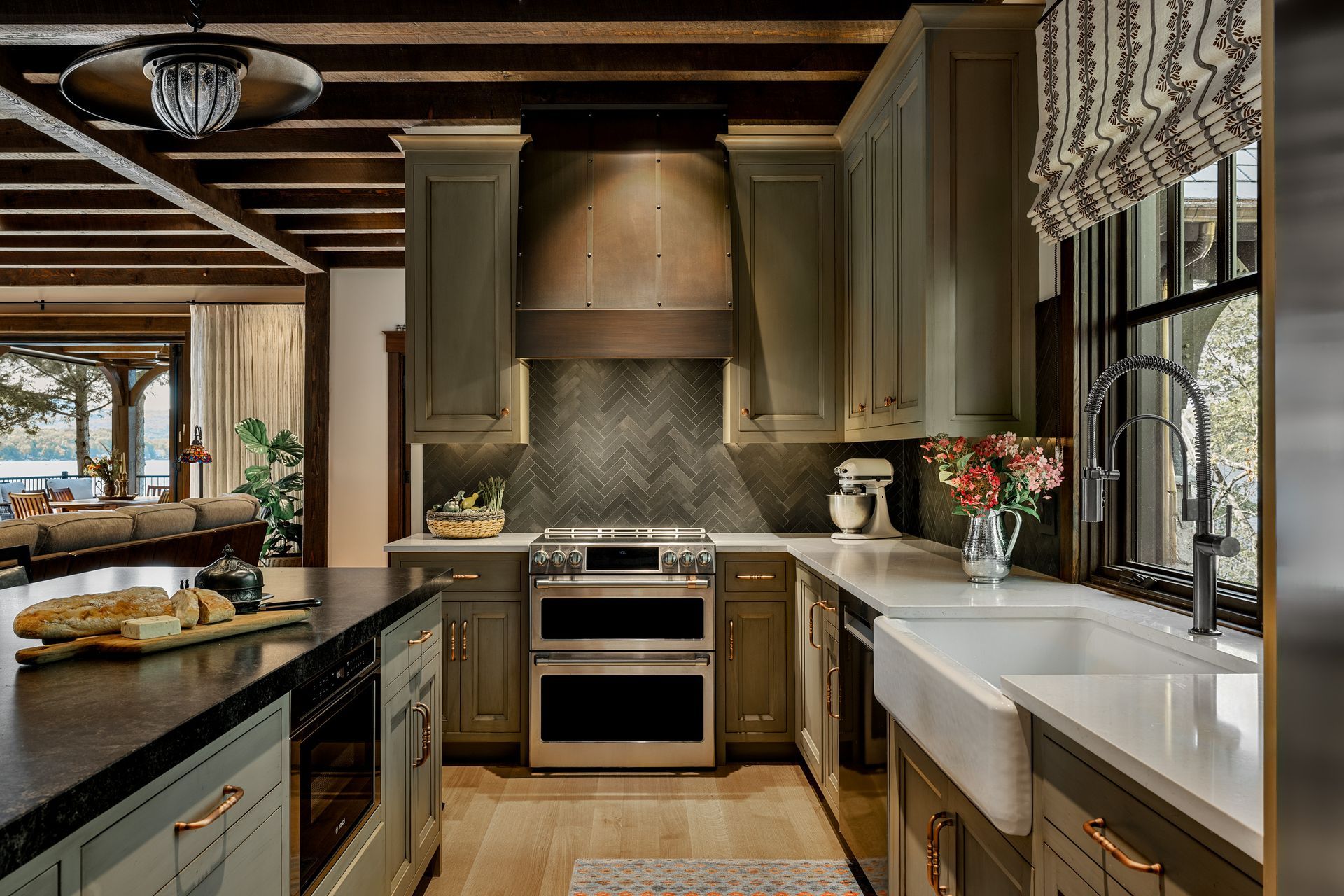 A kitchen with sage green cabinets, stainless appliances, a herringbone tile backsplash, and a farmhouse sink.