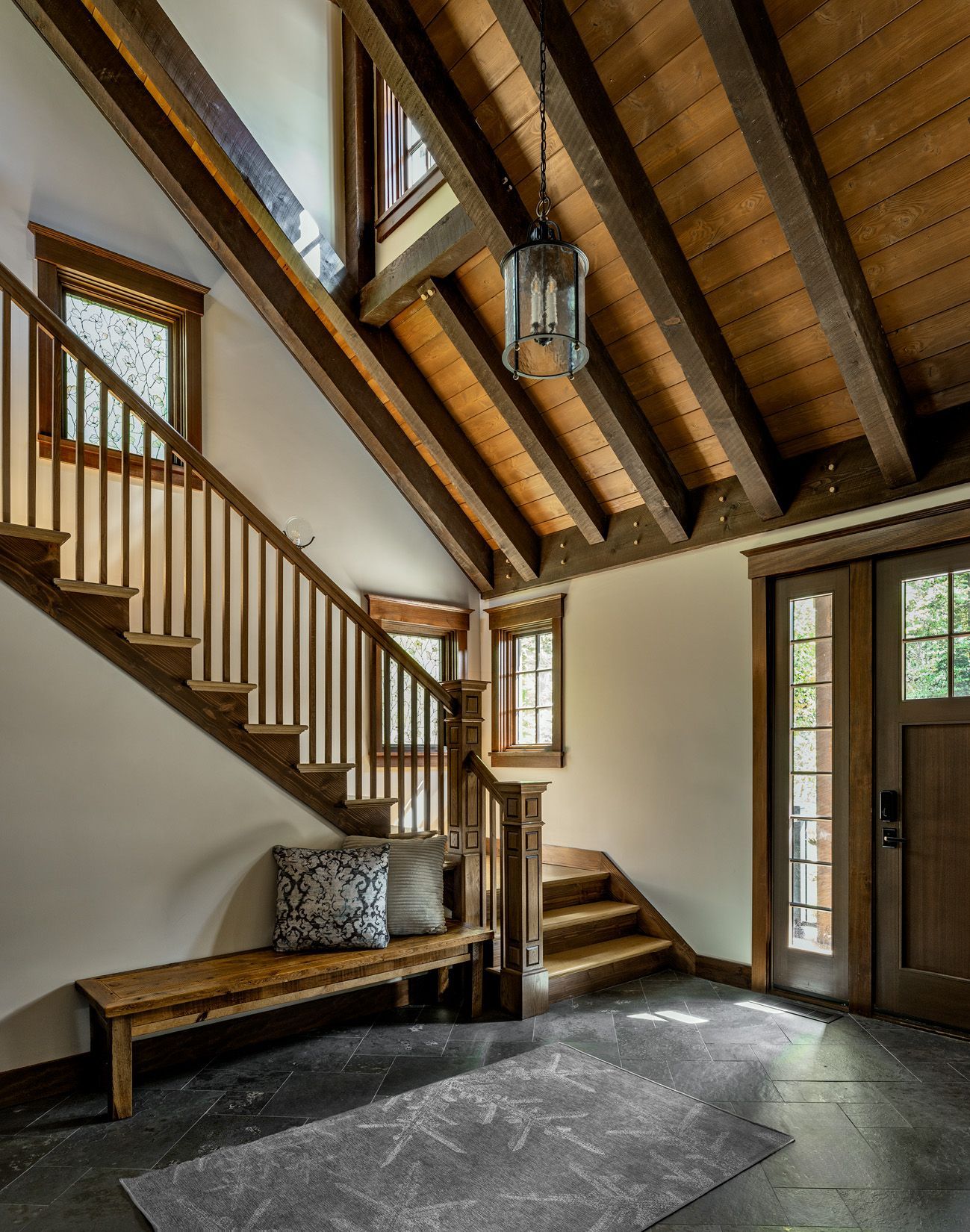 Foyer with stone flooring, wooden staircase, vaulted ceiling with exposed beams, and a bench under the stairs.