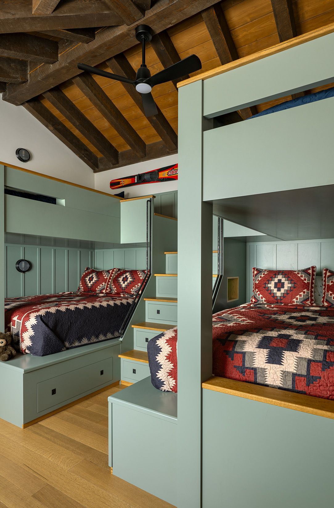 Custom built-in bunk beds in light green, featuring patterned quilts, wooden ceilings, and a ceiling fan.