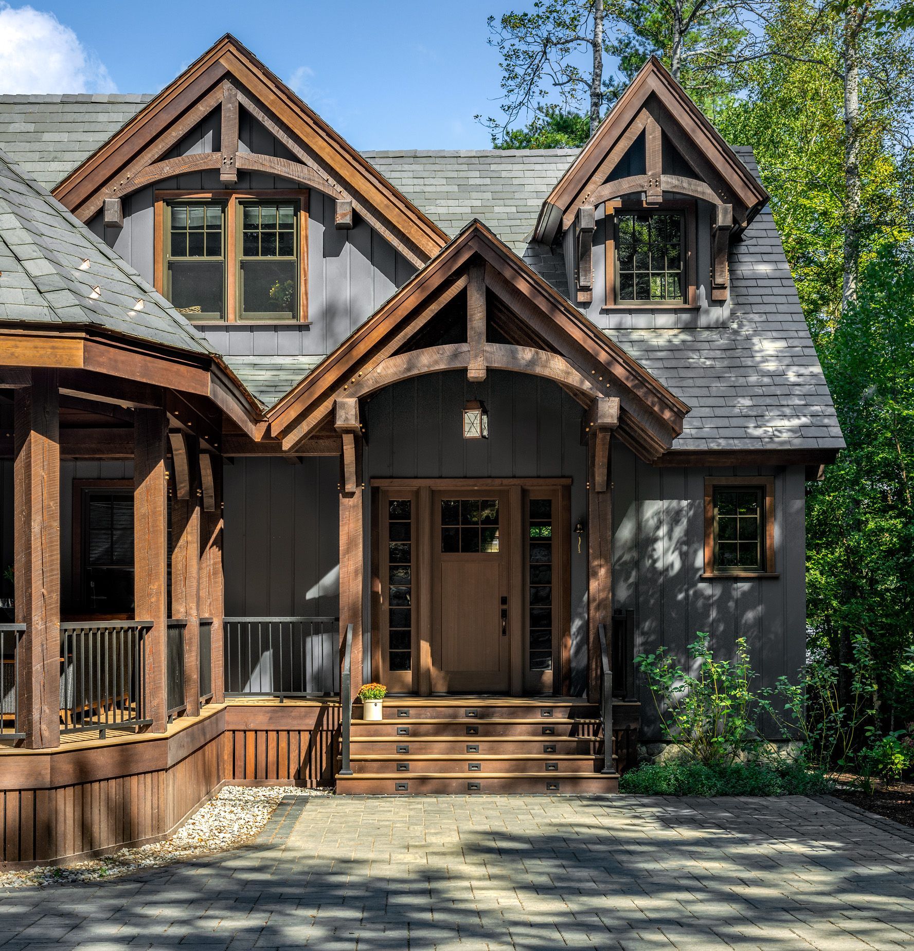 A wooden-trimmed house with gray board-and-batten siding, featuring a gabled porch entrance and a stone-paved driveway.