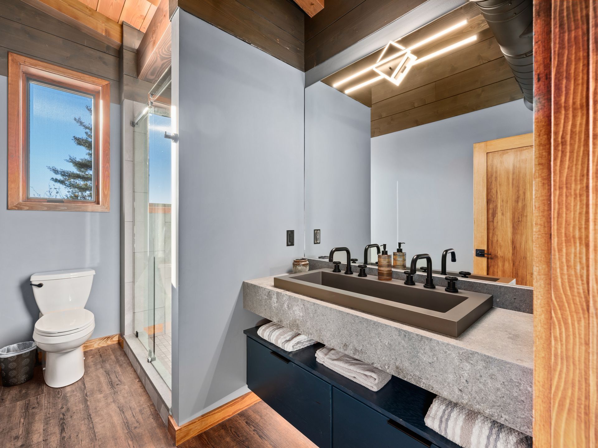 Modern bathroom with a floating concrete vanity, black rectangular sink, and a glass-enclosed shower on wood flooring.