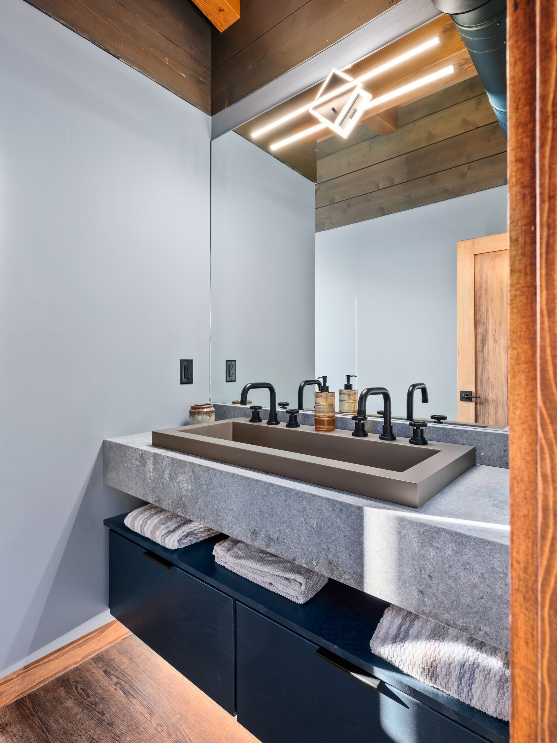 A modern bathroom vanity featuring a rectangular gray stone sink, dark blue cabinets, and a large mirror with warm lighting.