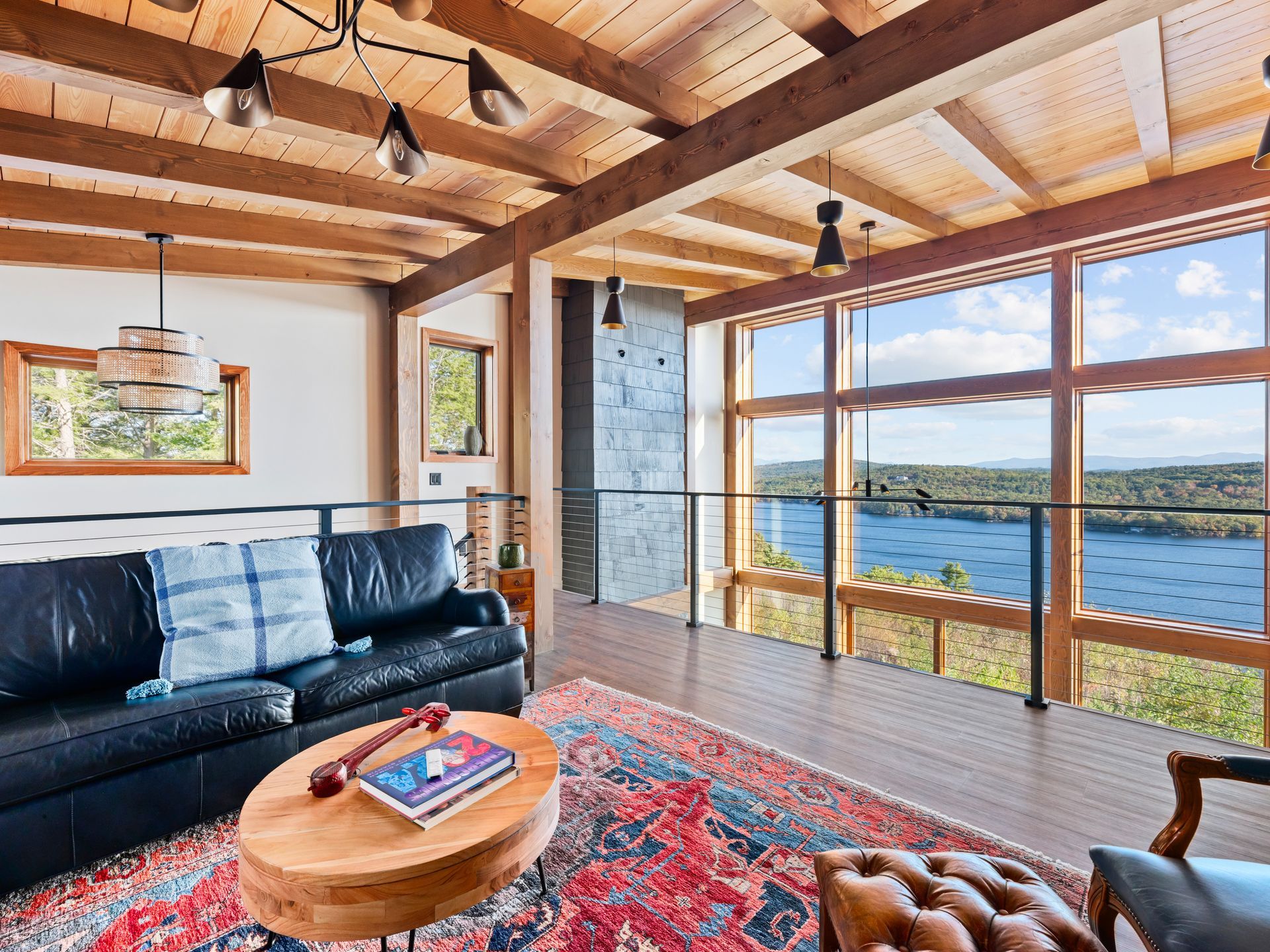 A living area with a leather sofa, oval wood coffee table, and patterned rug, featuring floor-to-ceiling views of a lake.