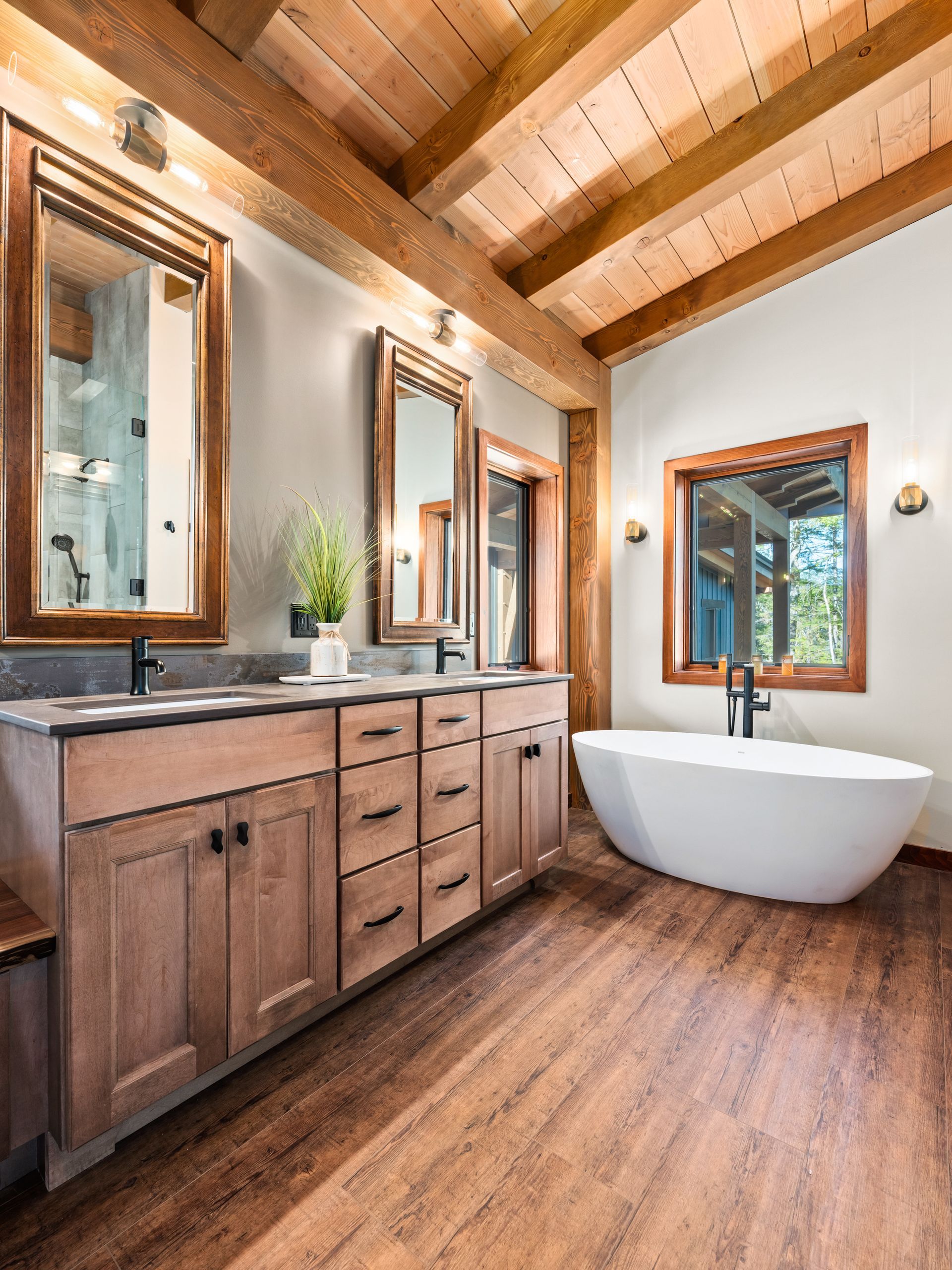 Rustic bathroom with wood-beamed ceiling, double vanity with mirrors, and a freestanding white bathtub.