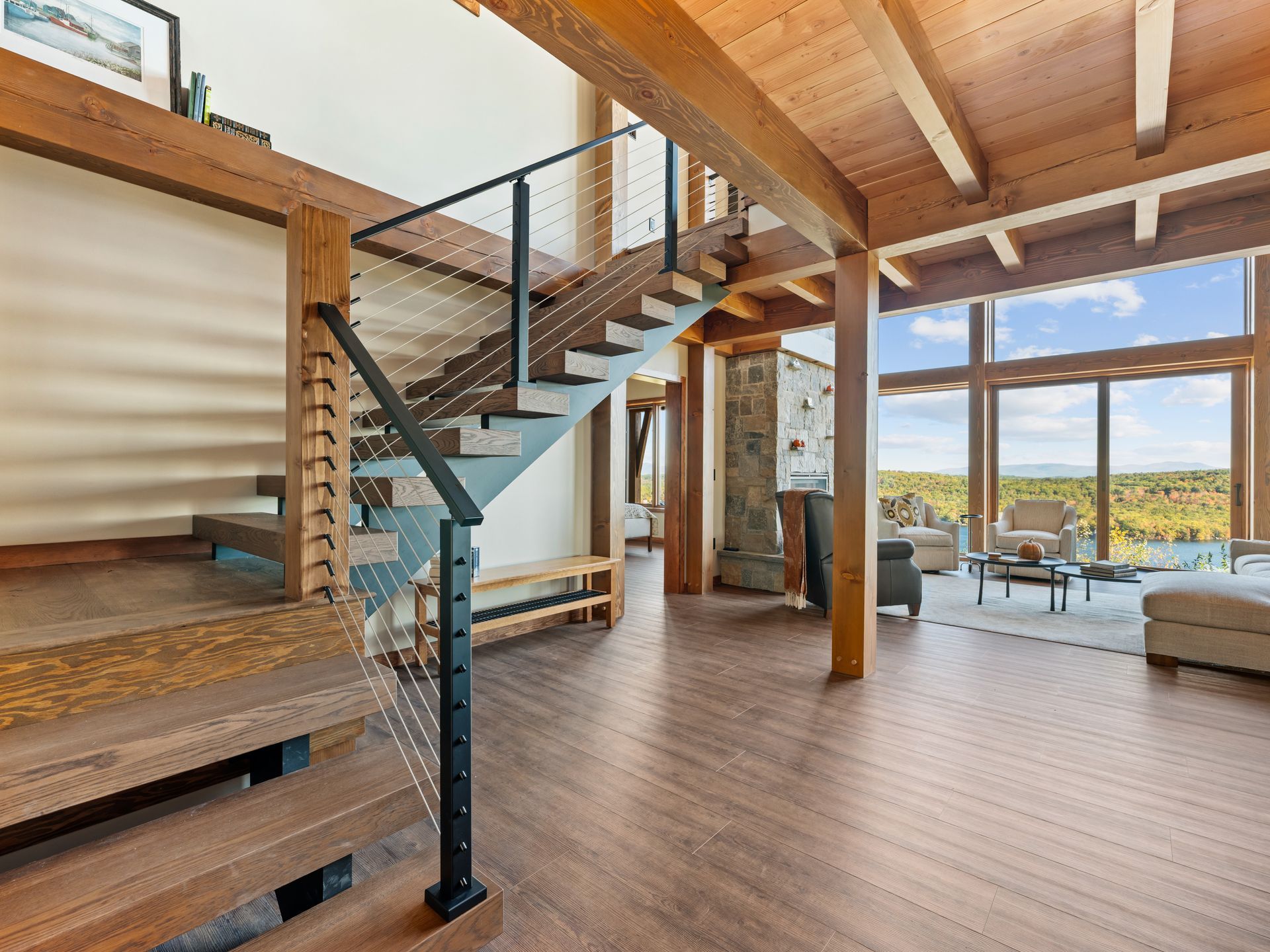 A staircase with wooden treads and cable railings inside a modern, open-concept home with floor-to-ceiling windows.