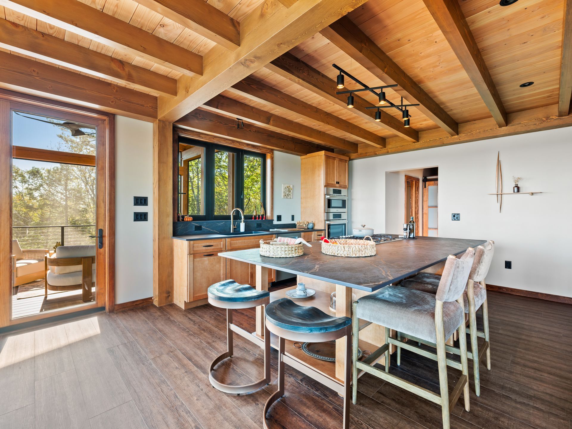 A modern kitchen with wooden beams, a large stone island with bar stools, and a glass door leading to a balcony.