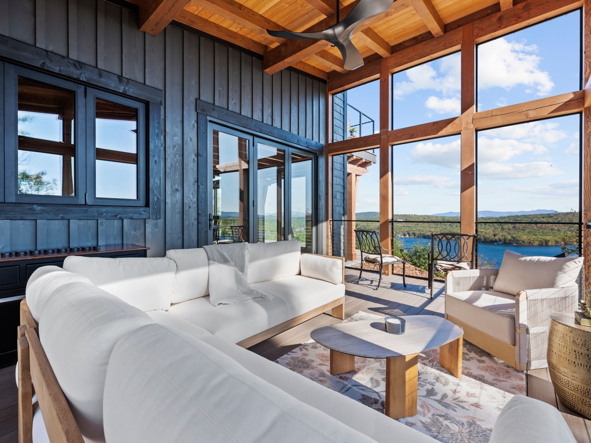 A sunroom with white sofas and a coffee table overlooking a lake through large floor-to-ceiling windows.