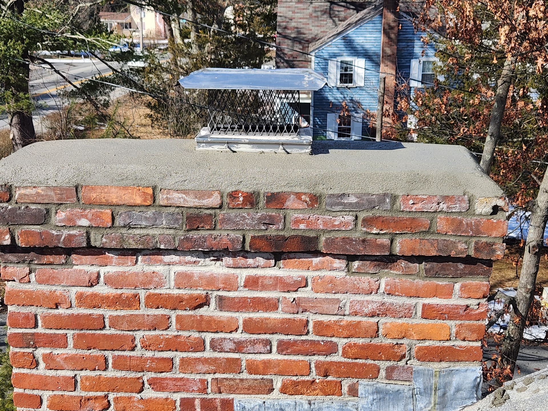 A brick chimney with a bird feeder on top of it in front of a blue house.