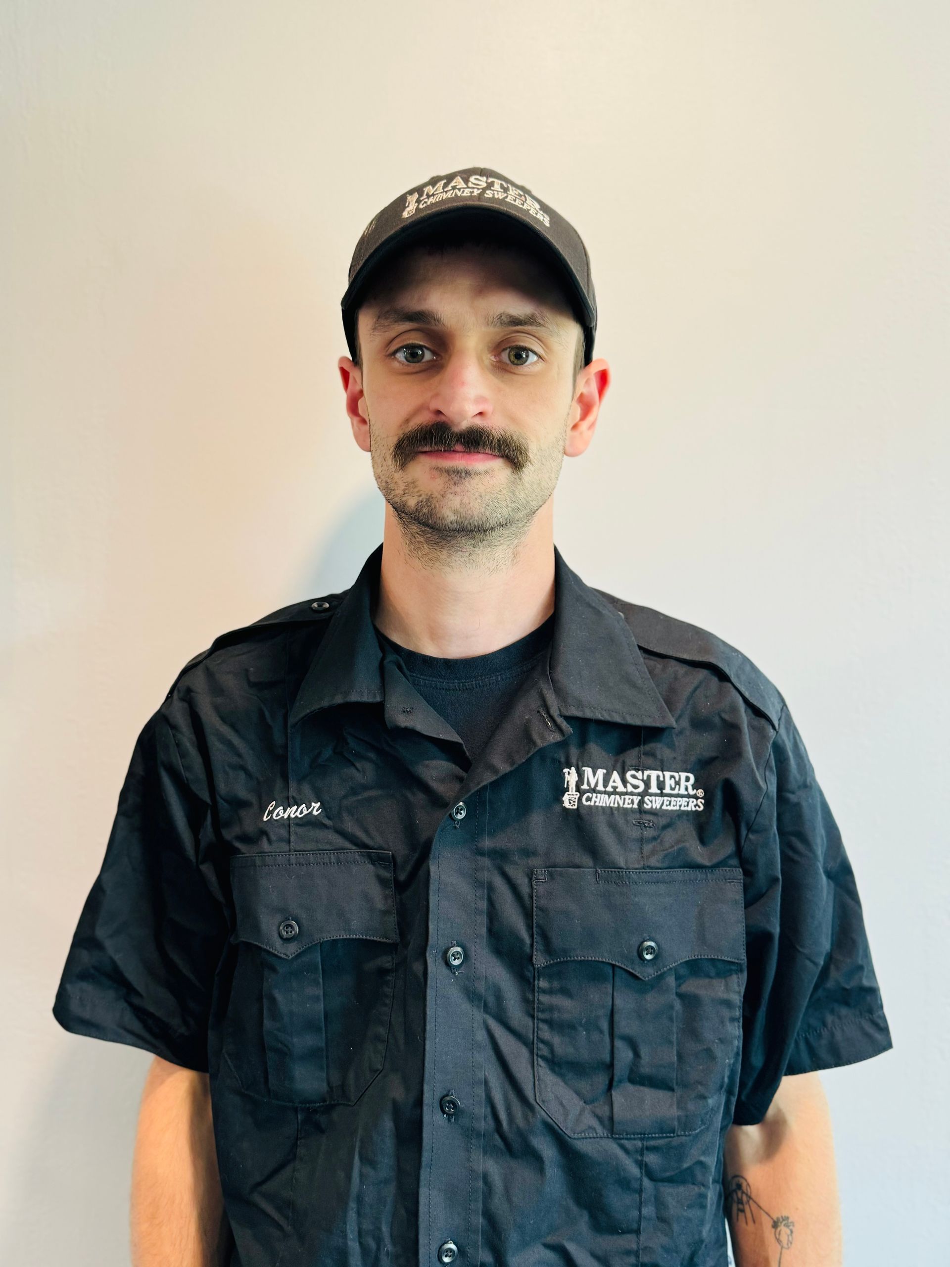 A man with a mustache is wearing a hat and a black shirt.