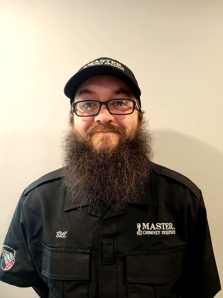 A man with a beard and glasses is wearing a hat and a black shirt.