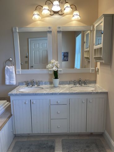 White double-sink vanity with mirrors, lights, and a cabinet in a bathroom.