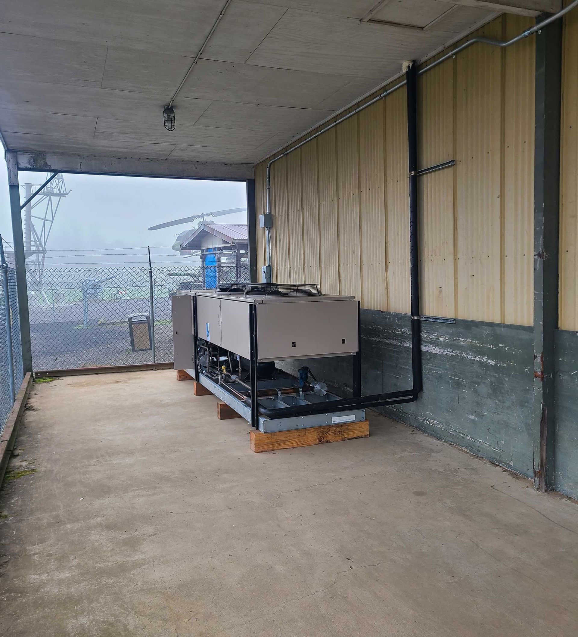 Large industrial chiller unit in an outdoor covered area with a chain-link fence visible.