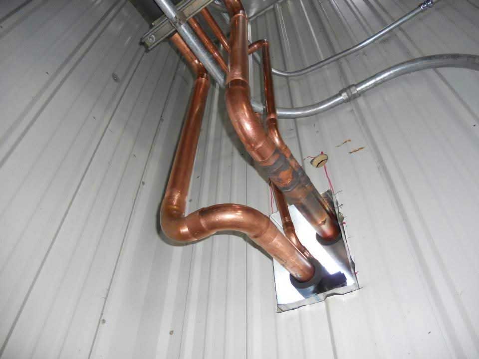 Copper pipes exiting a metal building through a square opening.