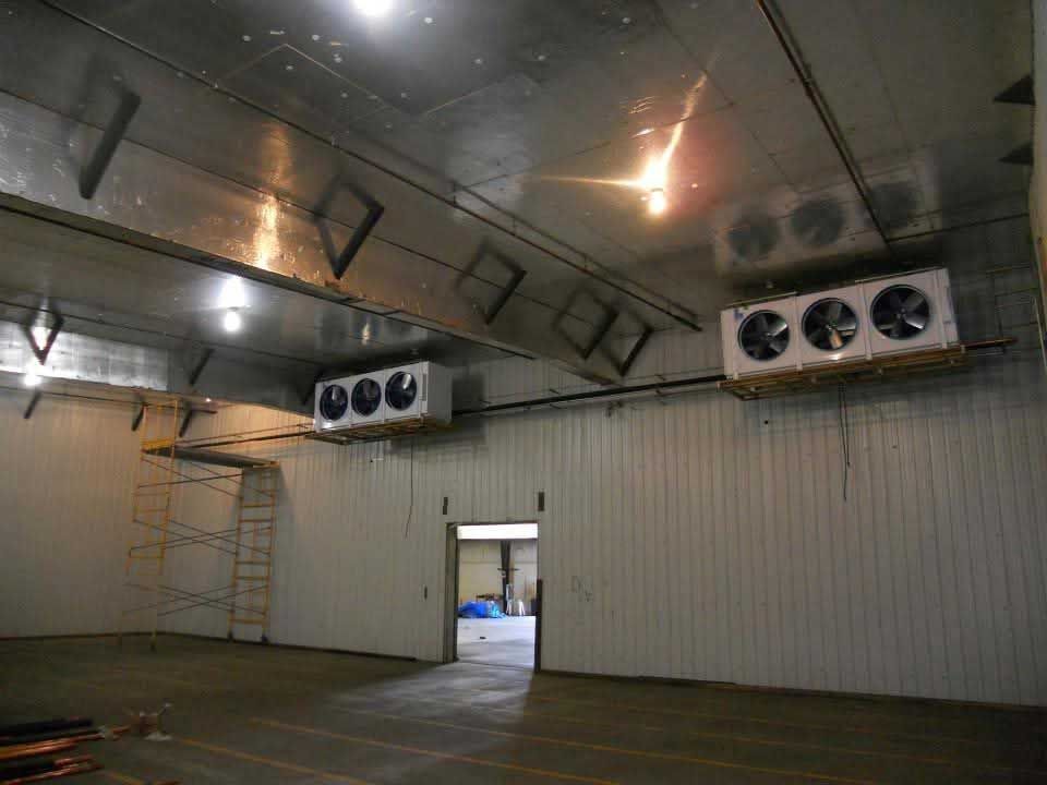 Interior of a large, empty cold storage room with multiple cooling units mounted on the walls.