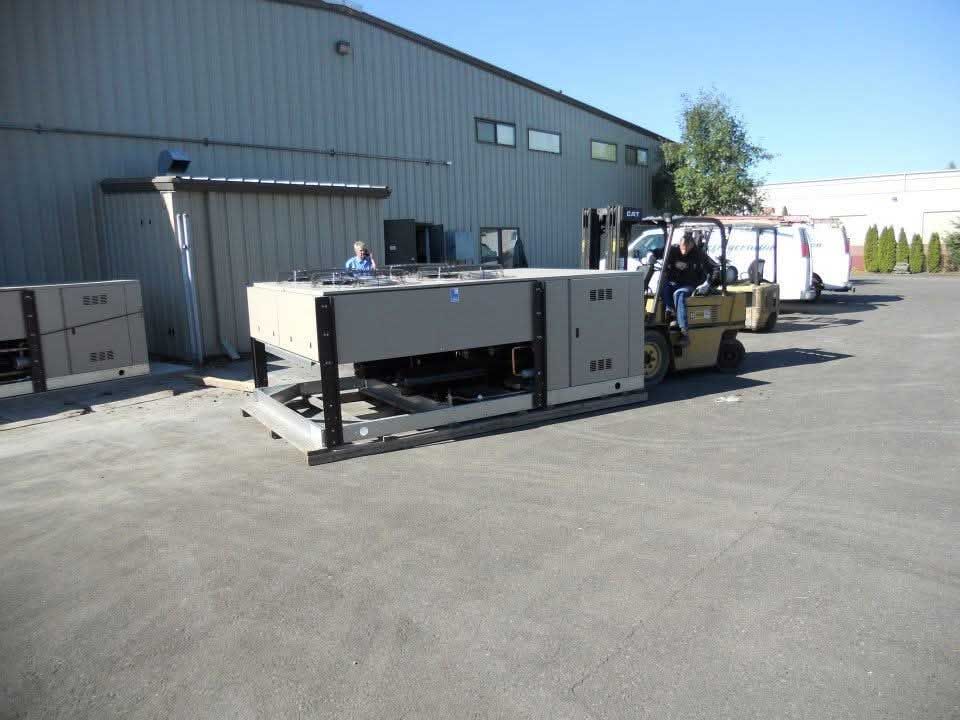 Forklift moving large equipment near a warehouse.