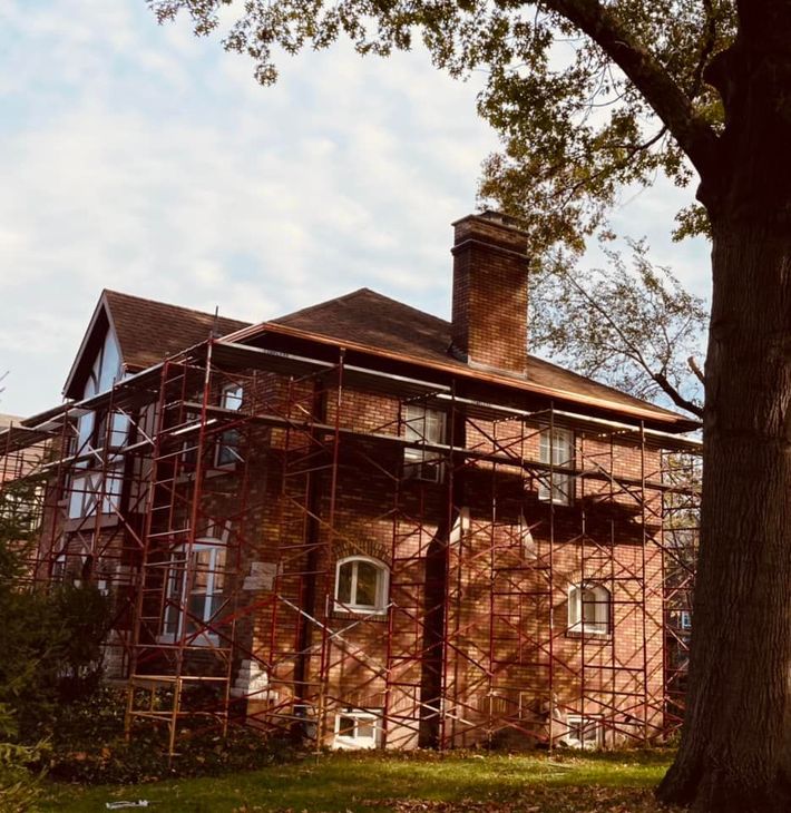 A brick house with scaffolding around it and a tree in front of it