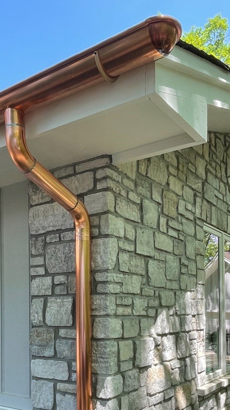 A man on a ladder is working on a copper pipe on the side of a building.