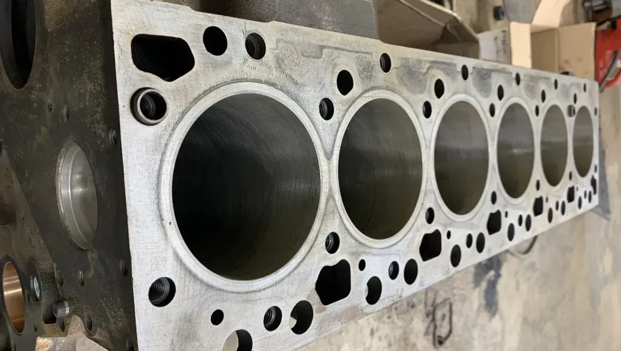 Engine block with seven cylinder bores visible. Steel color with bolt holes.