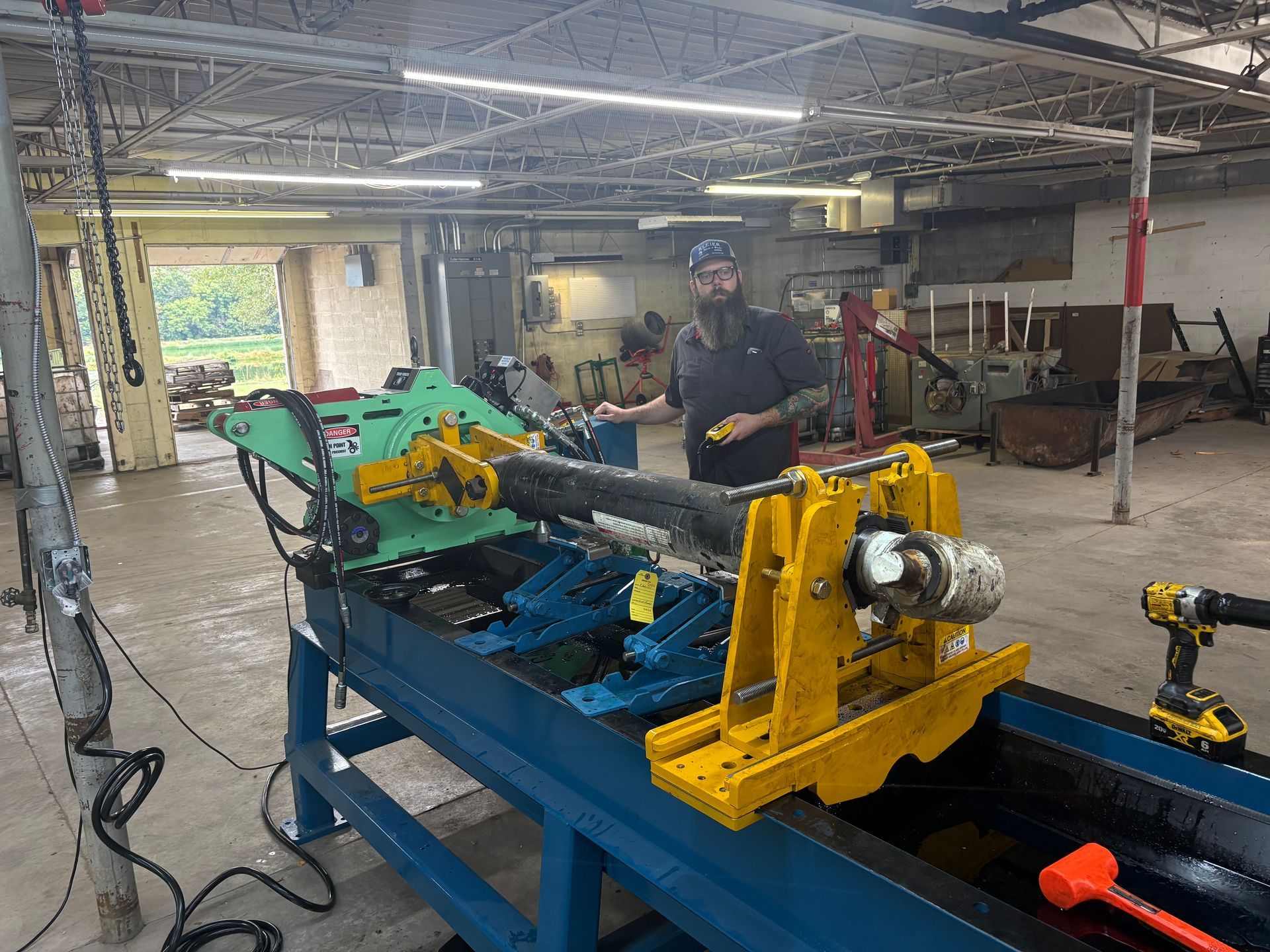 Man working on machinery in a workshop. A long metal piece is held by yellow supports on a blue table.