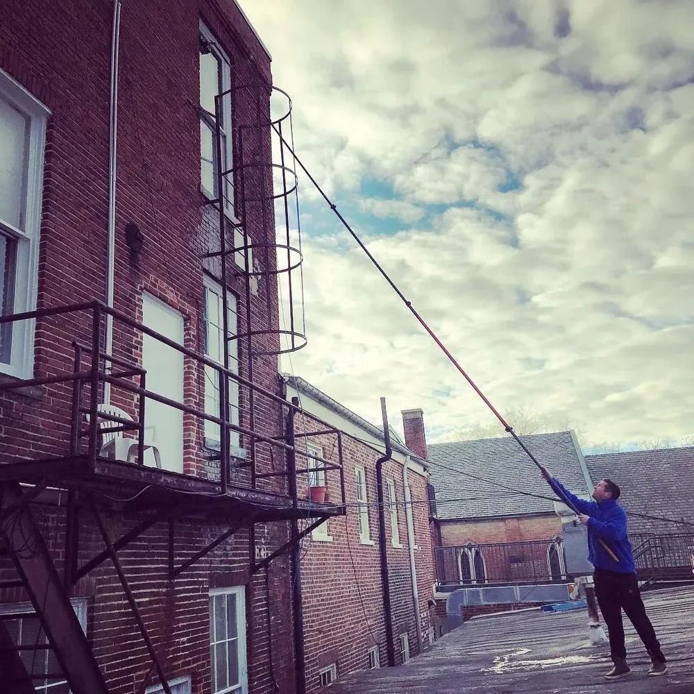 Person using a long pole to reach a brick building exterior under cloudy sky