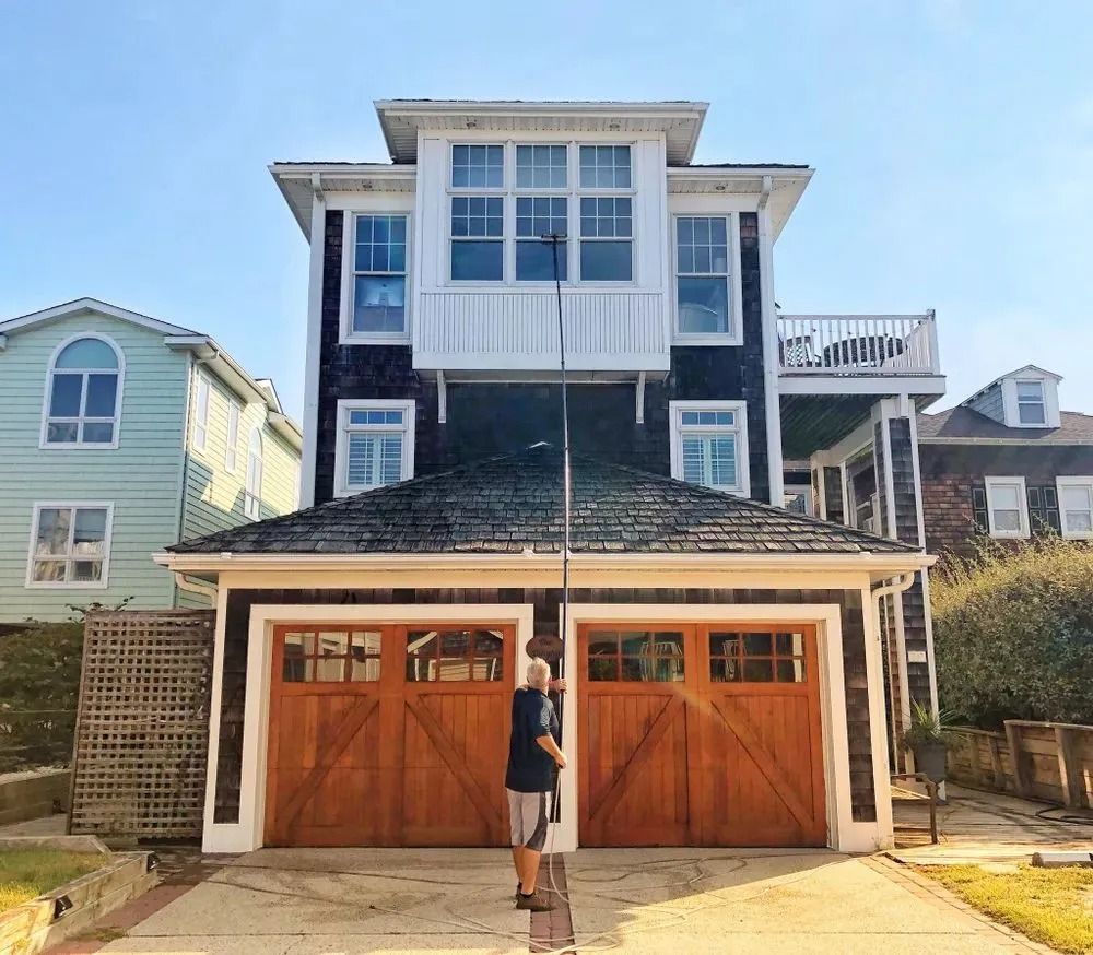 Two-story beach house with gray siding, white trim, and double wooden garage doors; person standing in front.
