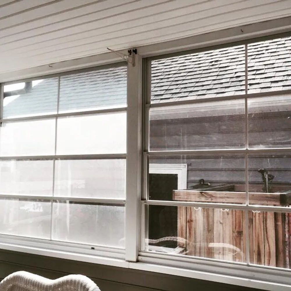 Sliding glass windows with white blinds overlooking an outdoor patio and wooden fence