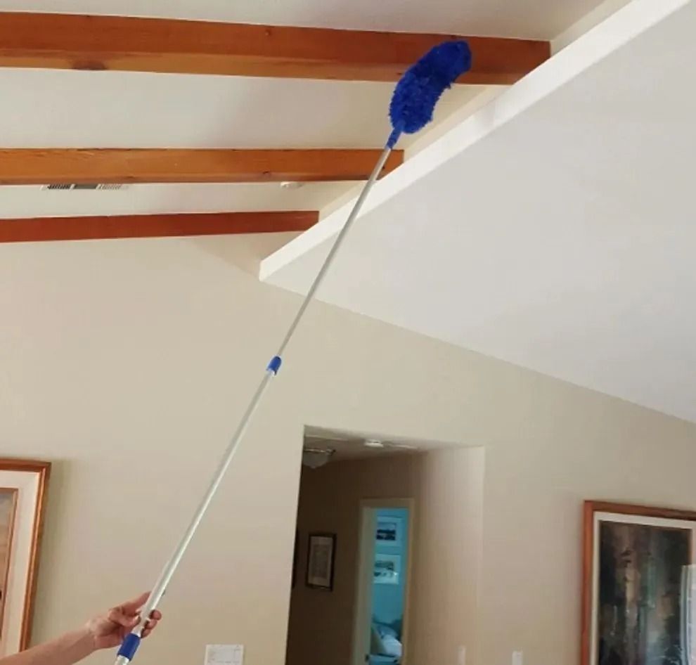 Person using a long blue duster to clean ceiling beams in a living room