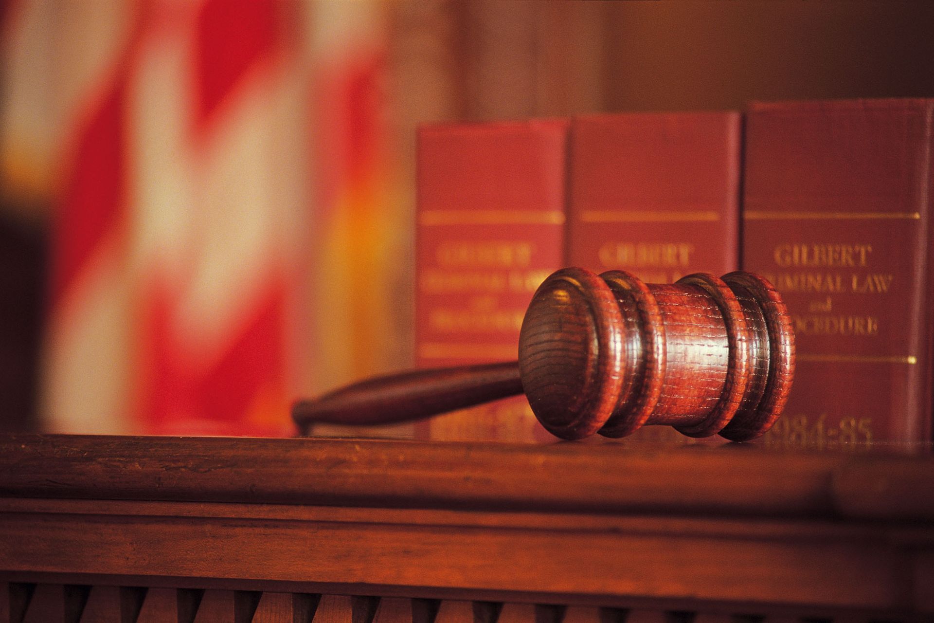 Gavel on wooden surface in front of law books and blurred American flag.