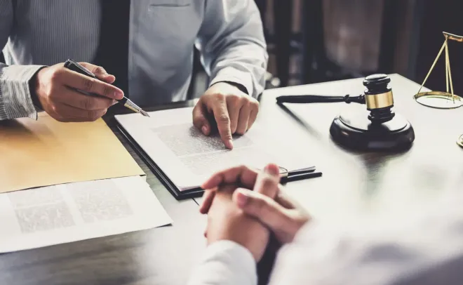 Lawyer pointing to document, discussing with client, gavel and scales on desk.