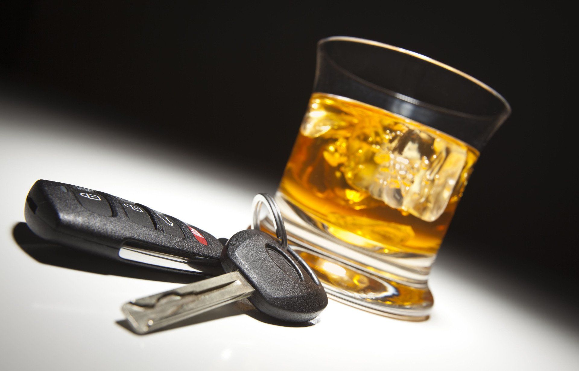 Car keys next to a glass of whiskey with ice, against a dark background, representing drunk driving.
