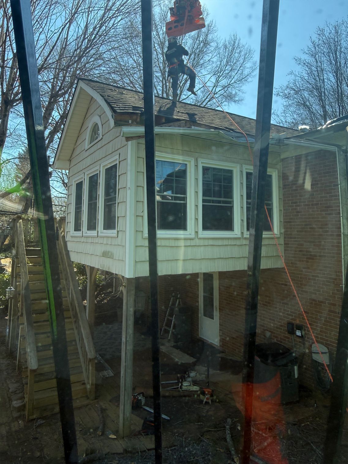 House with elevated section; person on roof, possibly repairing shingles. Brick and wooden construction.