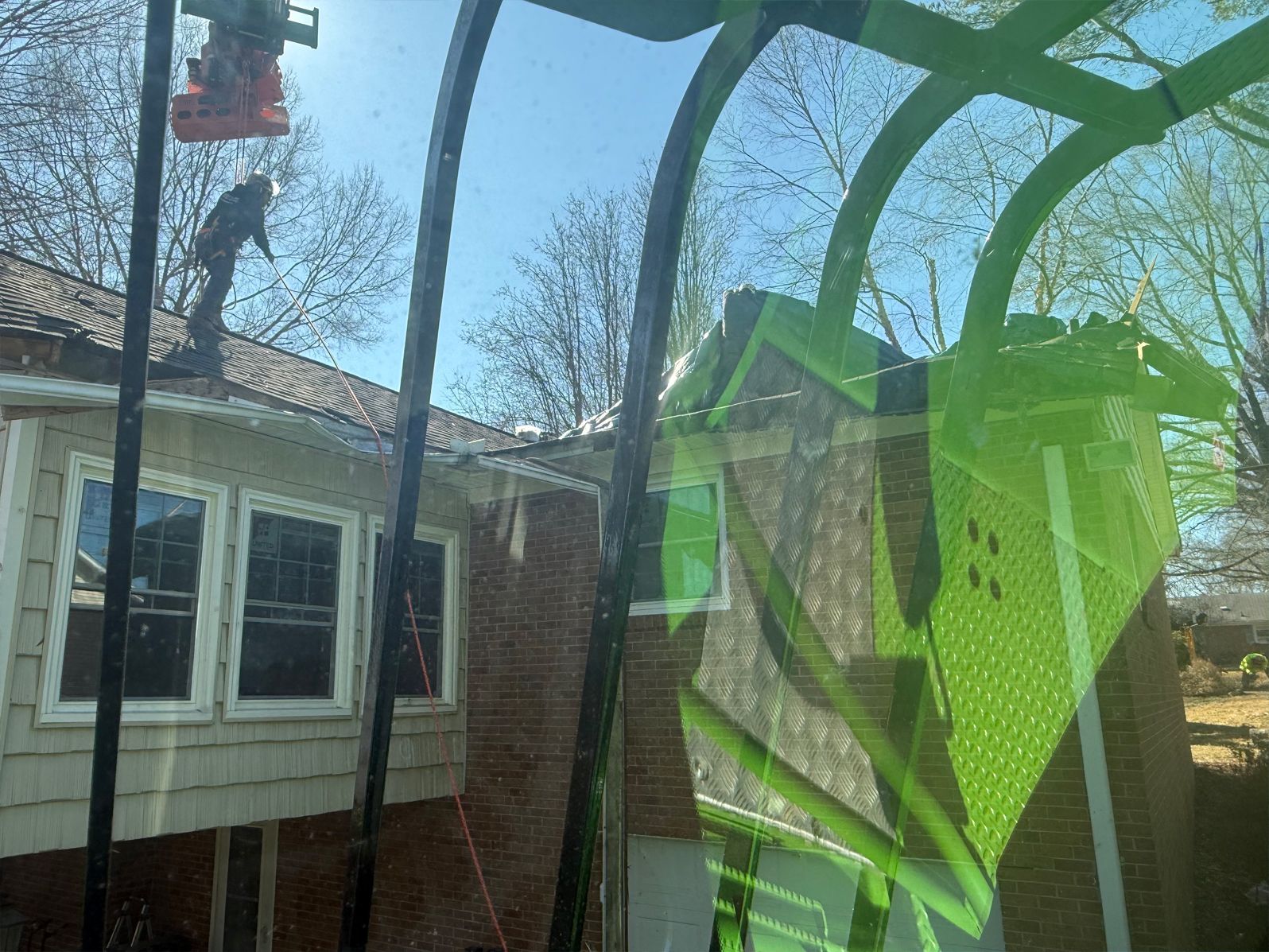 Person on roof repairs. Brick house, sun, green arch reflection.