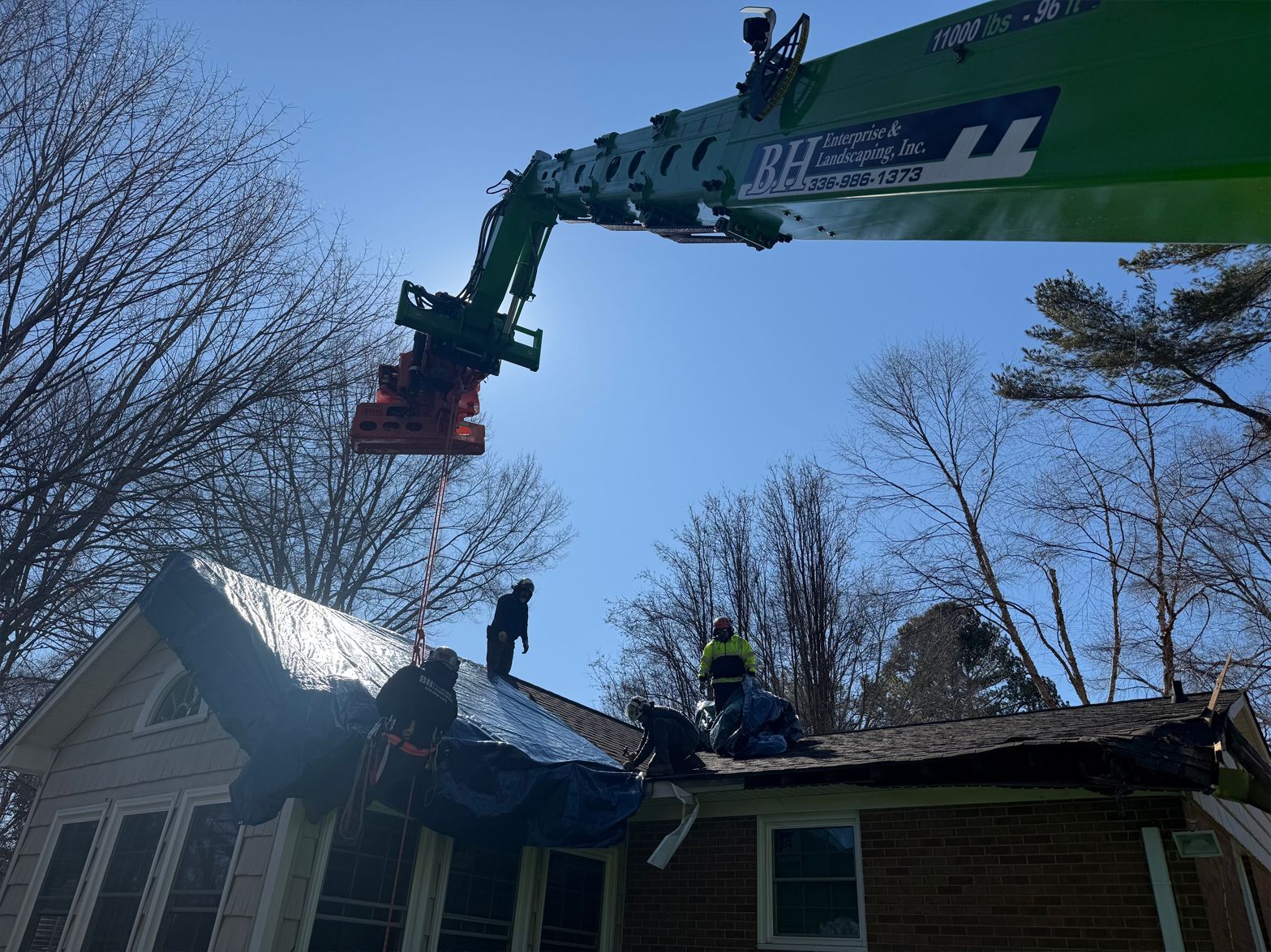 Construction workers on a house roof being demolished by a large crane. Blue sky overhead.
