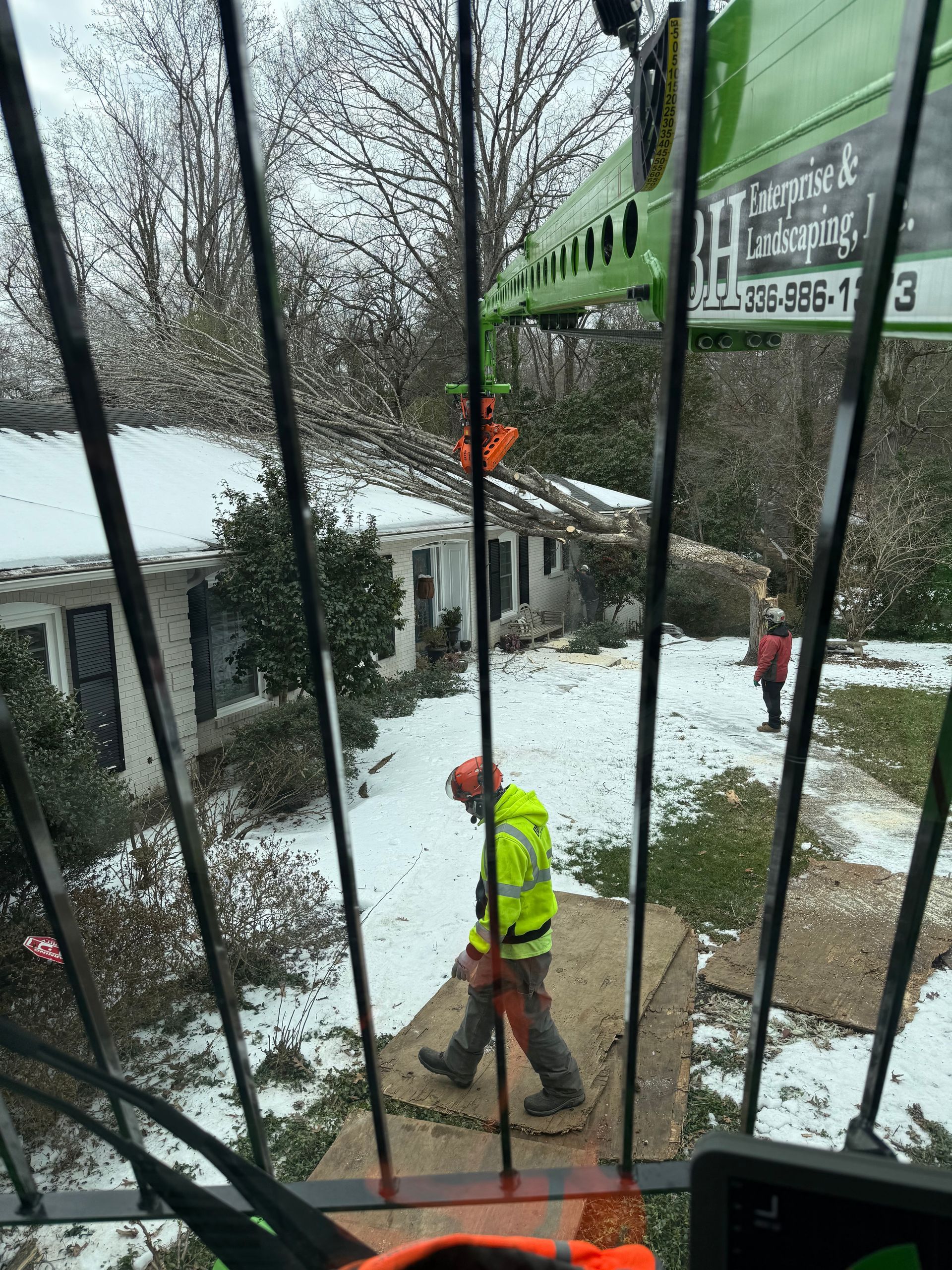 Worker in safety gear walks towards a house covered in snow, crane overhead.