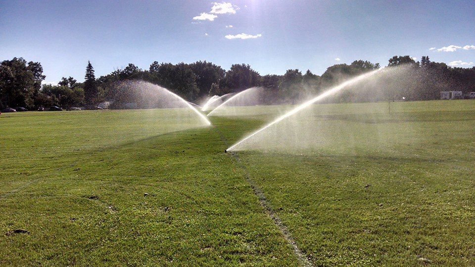 Two sprinklers are spraying water on a lush green field.