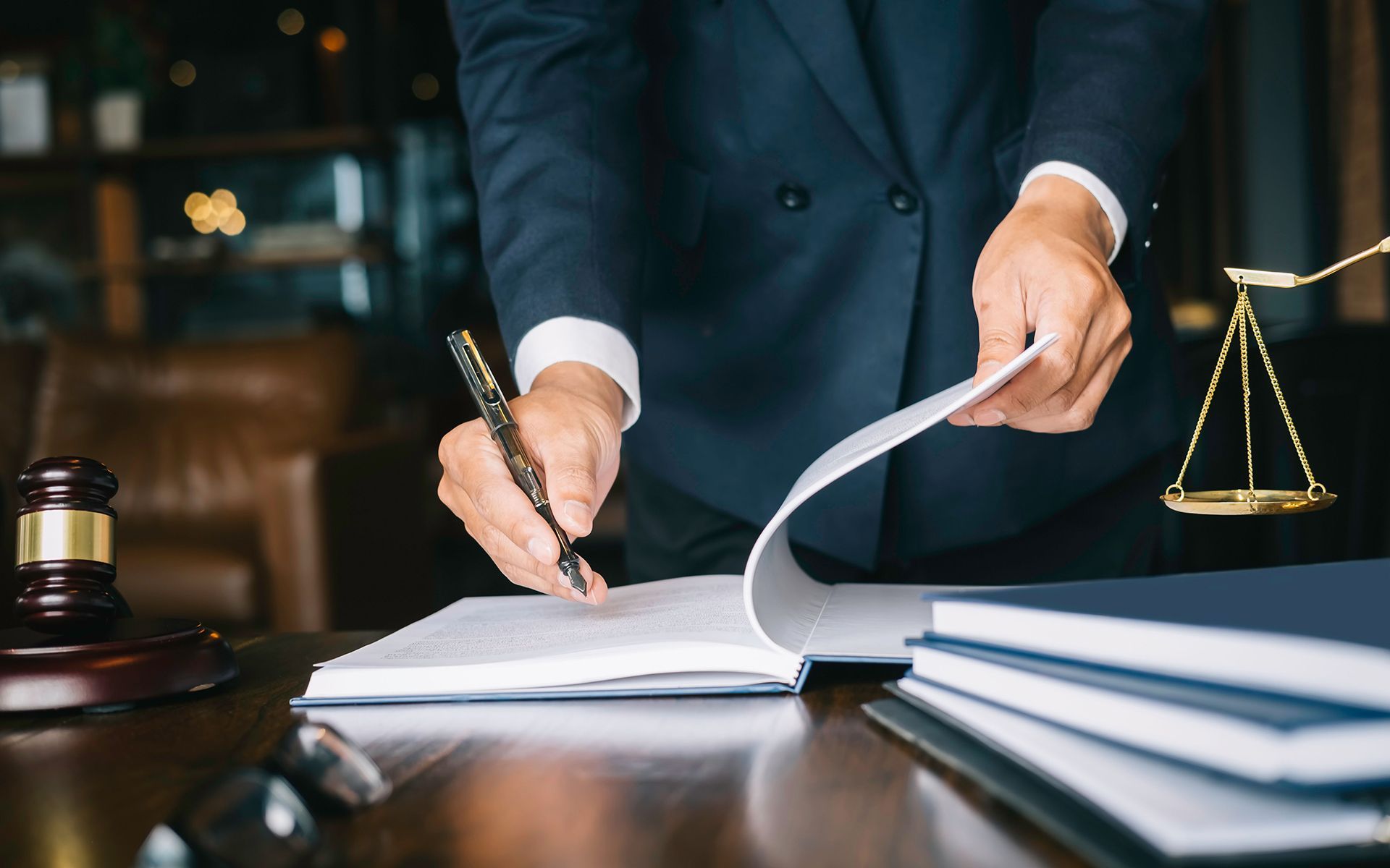 Lawyer signing documents at a desk with a gavel and scales of justice nearby