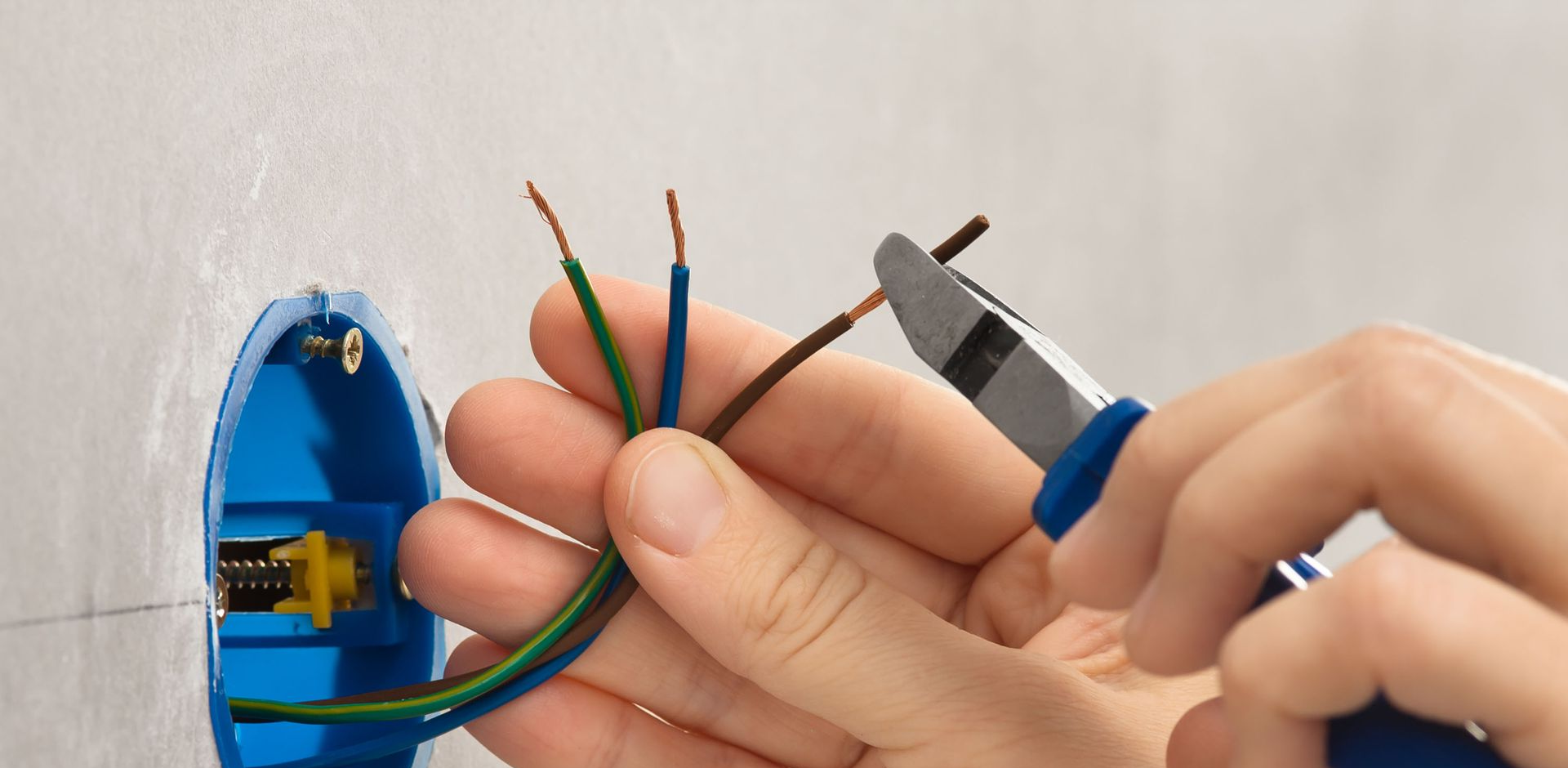 Hands wiring a blue electrical junction box with exposed colored cables and a utility knife.