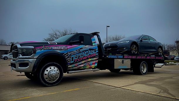 A tow truck is towing a car in a parking lot.