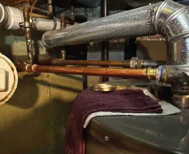 Copper pipes and heating vent near a water heater in a basement.