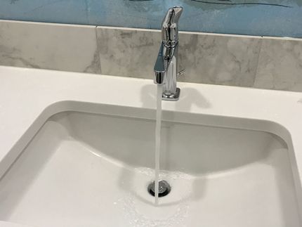 Faucet with water running into a white sink in a bathroom.