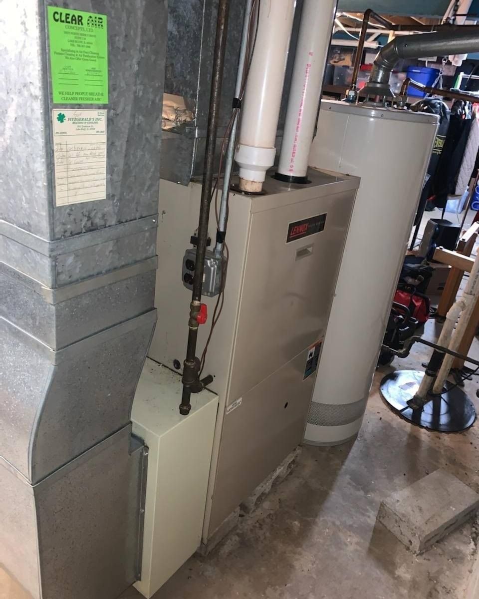 Furnace and water heater in a basement. Ductwork is to the left. Pipes and electrical components are visible.