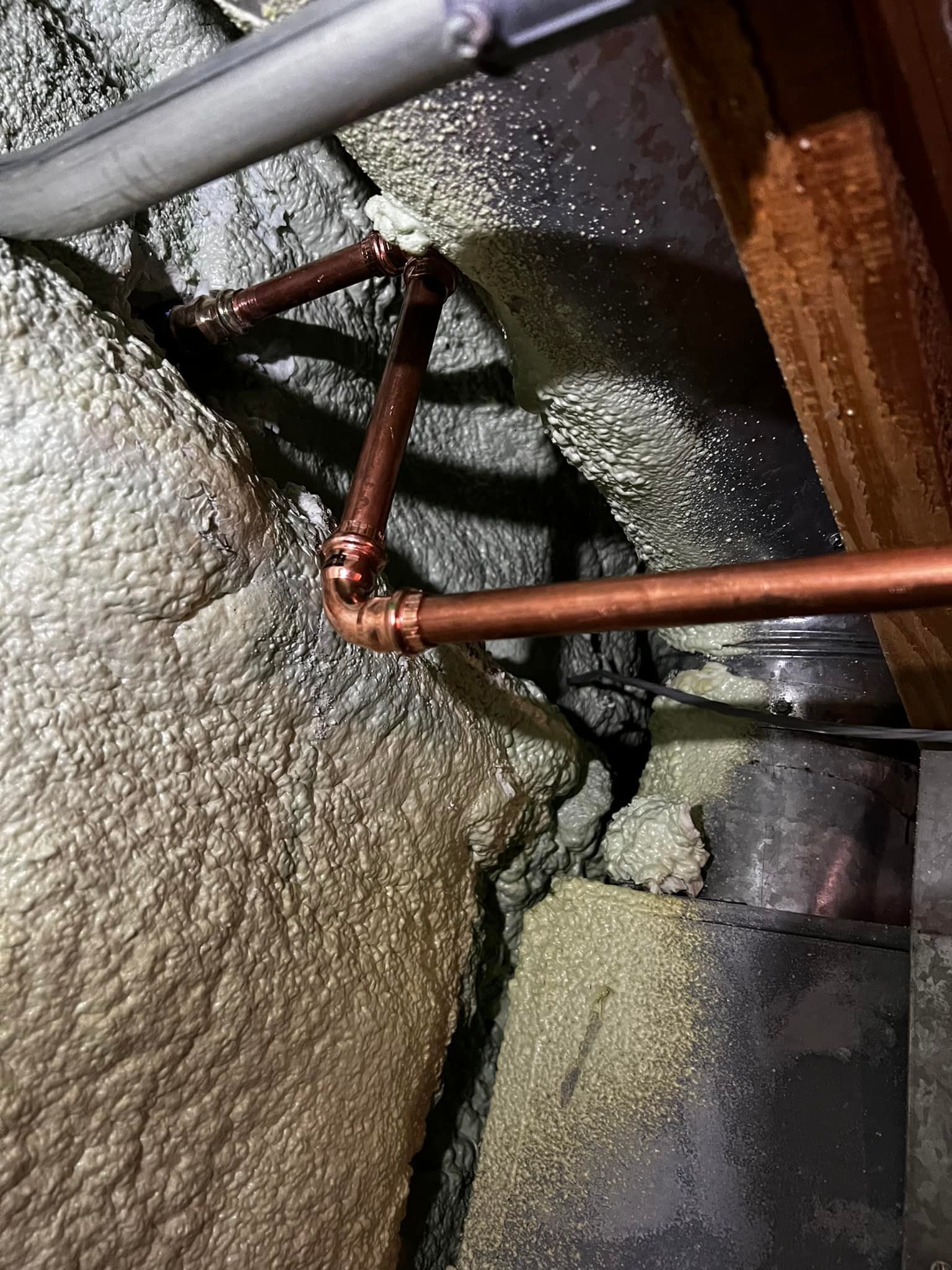 Copper pipes and fittings connected in an insulation-filled space near ductwork and wood framing.