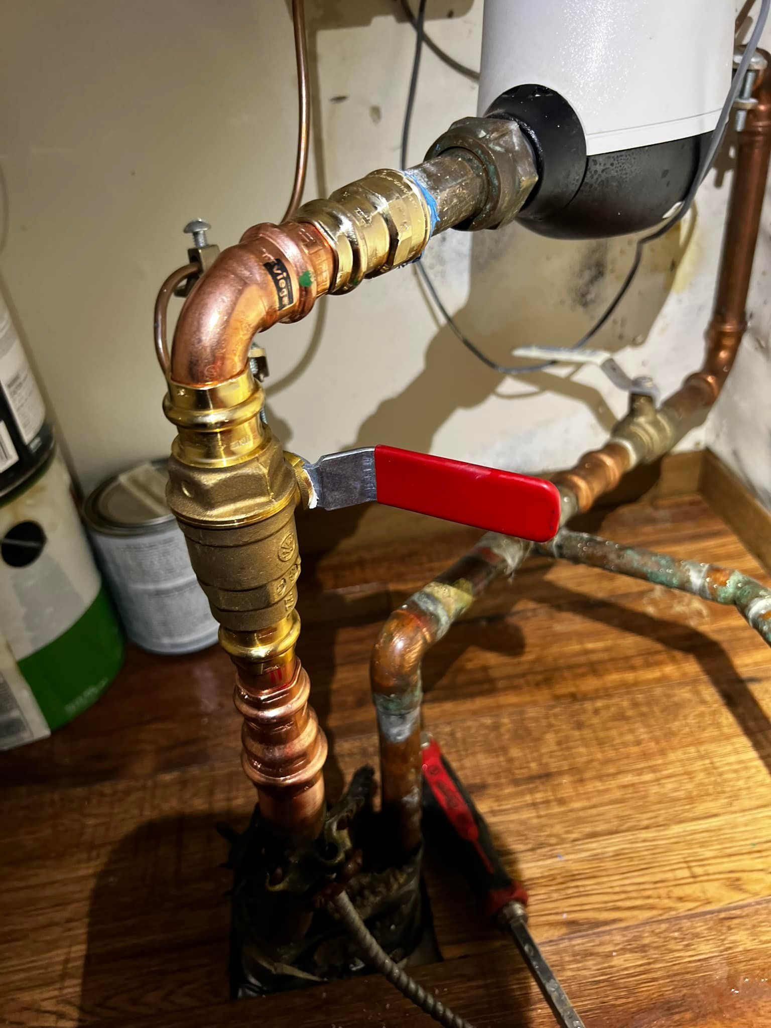 Copper pipes and a brass valve with a red handle in a basement.