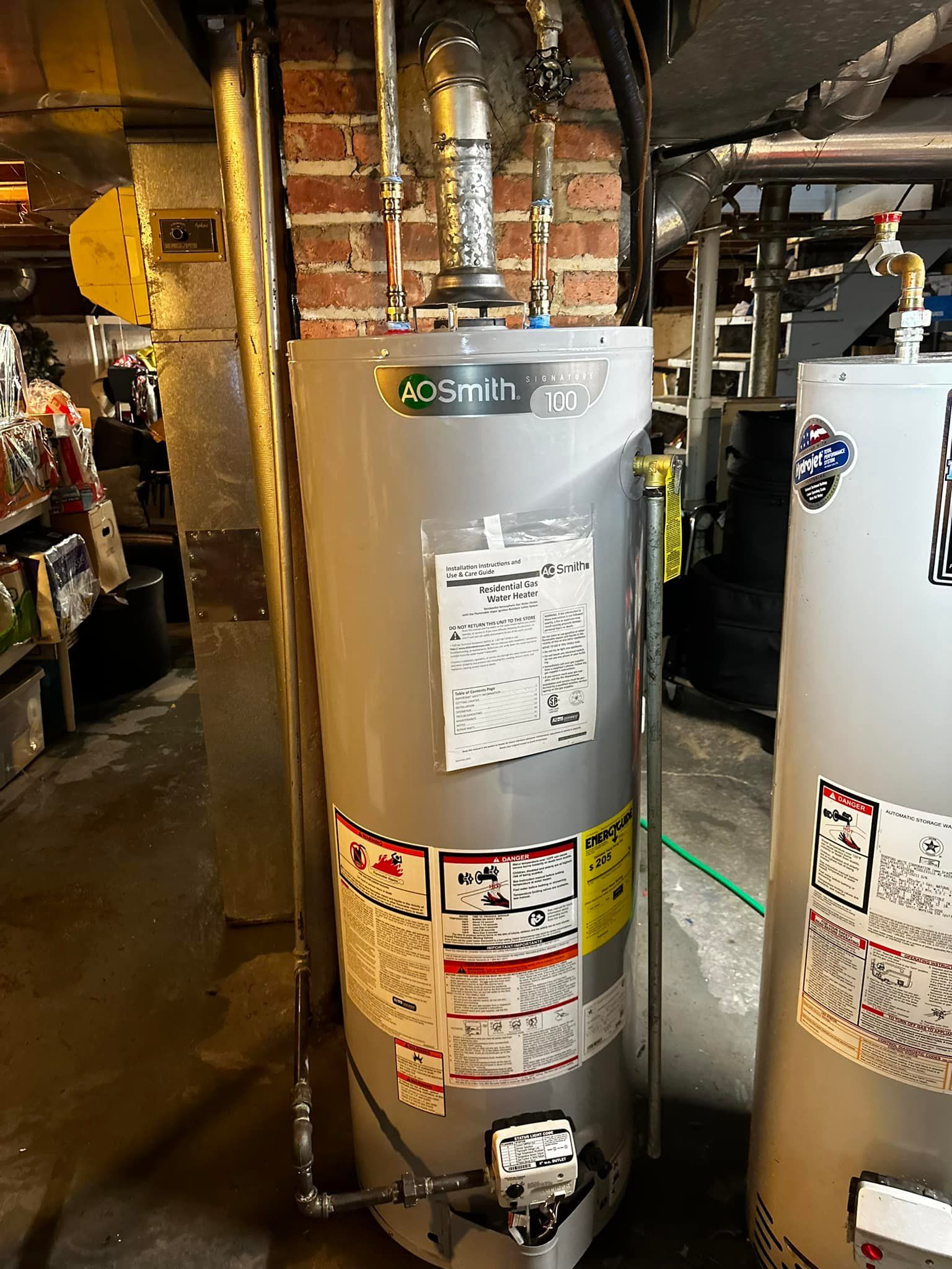 A.O. Smith water heater in a basement setting with various pipes and stickers attached to its surface.